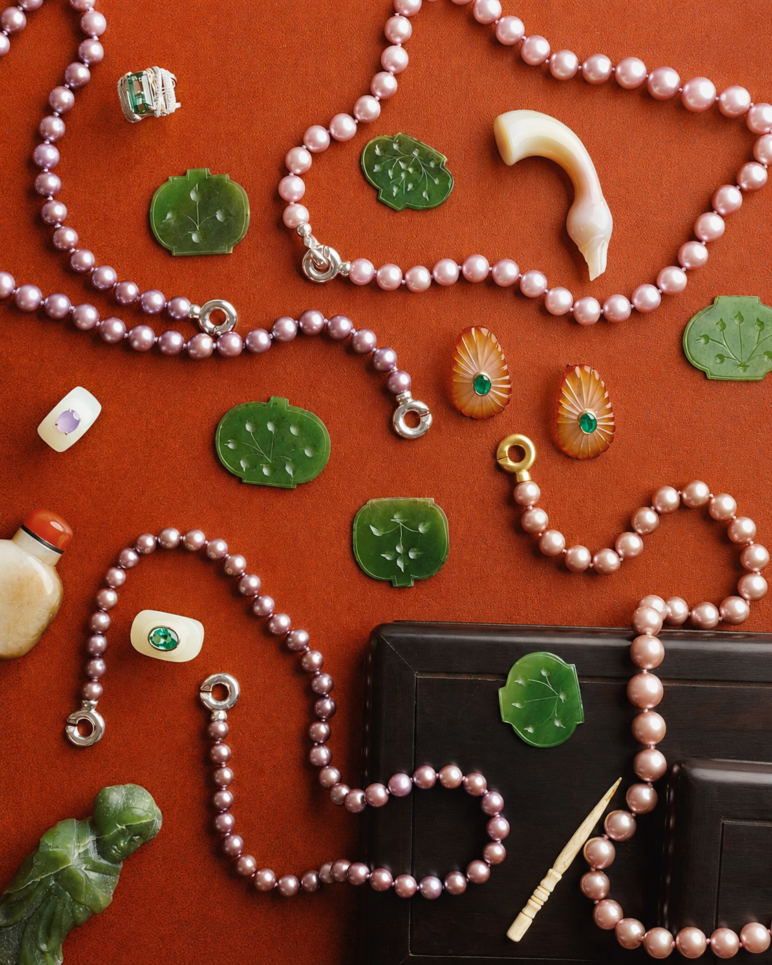Jade carvings, pearl strands and an agate horn arranged on a terracotta ground