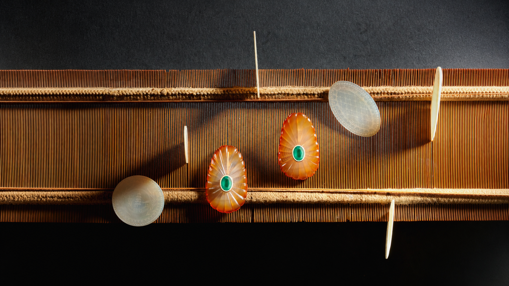 Carved agate and mother-of-pearl objects laid across a woven loom